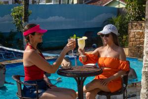 dos mujeres sentadas en una mesa junto a una piscina con una bebida en Namoa Pollastrini, en Itanhaém