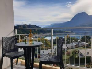 einen Tisch mit 2 Stühlen und eine Flasche Wein auf dem Balkon in der Unterkunft Superbe appartement avec vue sur lac et montagnes - Station de ski 10 min in Chorges