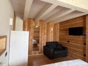 a bedroom with wooden walls and a chair and a television at Camelot Luxury Houses Horses in Pellizzano