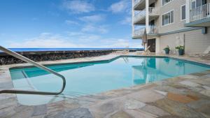 a swimming pool in front of a building with the ocean in the background at Beautiful Oceanfront Welcomes you at Hale Kona Kai 203 by Casago Kona in Kailua-Kona