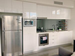 a kitchen with white cabinets and a stainless steel refrigerator at Cosy and Stylish 1 BD Serviced Apt at SouthBank in Brisbane