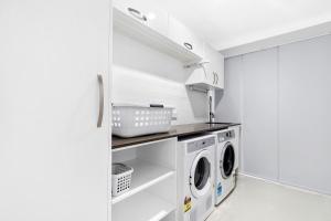 a white laundry room with a washer and dryer at Breathtaking 4BR Resort like House Right Near Wurtulla Beach With Infinity Pool in Kawana Waters