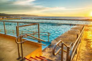 a swimming pool next to the ocean at sunset at Modern 2BR Apartment near Wollongong Beach in Wollongong