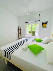 a white bedroom with a large bed with green pillows at Mahagedara Dickwella in Dickwella