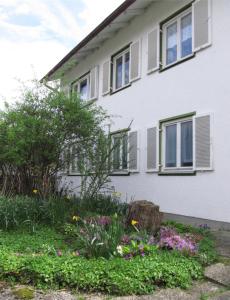 une maison blanche avec des fenêtres et des fleurs devant elle dans l'établissement Ferienwohnung Bluhm, à Weilheim in Oberbayern
