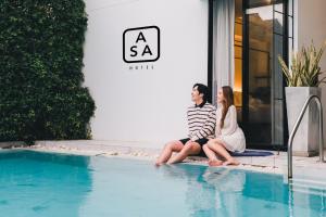 two women sitting next to a swimming pool at Asa Hotel in Chiang Mai