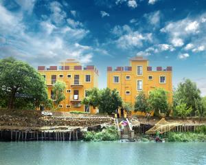 une rangée de bâtiments jaunes à côté d'une masse d'eau dans l'établissement Resort Neel Nirjan, à Bolpur