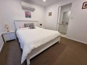 a white bedroom with a white bed and a night stand at Glass House Mountains Retreat in Beerwah