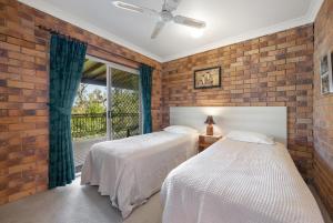 two beds in a bedroom with a brick wall at Coucals Cottage in Mount Crosby