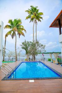 a swimming pool with palm trees and the water at Seclude by the Lake, Alleppey in Alleppey