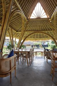a restaurant with tables and chairs and a straw roof at Nadi Nature Resort - Adults Only in Tabanan