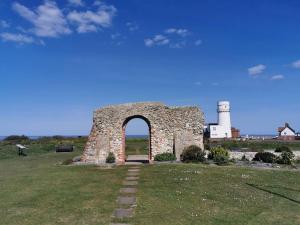 une arche dans un champ avec un phare en arrière-plan dans l'établissement Spacious Family Friendly Apartment- 100m from beach with Seaviews!, à Hunstanton