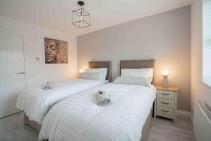 two beds in a bedroom with white sheets and a table at 2 Bed Home - HS2, NEC, Resorts World & BHX Airport in Marston Green