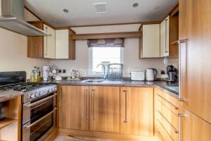 a kitchen with wooden cabinets and a stove top oven at Lovely Caravan For Hire With Decking At Skipsea Sands In Yorkshire Ref 41015wf in Barmston