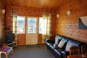a living room with a leather couch and a television at Woodland Hazel Lodge in Killin