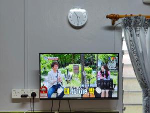 a tv with a clock on the wall and a tv screen with a woman talking at TBE Room2stay at Jalan BR3 in Melaka