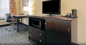 a hotel room with a television on a dresser with a desk at La Quinta by Wyndham McAlester in McAlester