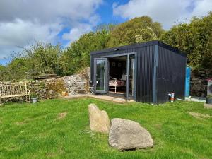a black shed in a yard with a rock in the grass at Rhubarb Hut, set in the beautiful Cornish Countryside in Helston