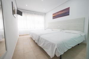 a white bedroom with two beds and a window at Hotel Pinar Somo Surf in Somo