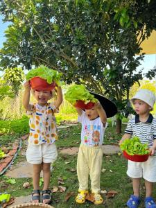 three children are holding pots of lettuce on their heads at Homestay Vườn Trái Cây Nhiệt Đới VÔ ƯU GARDEN in Bao Loc