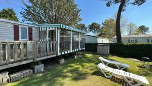a yard with two white benches and a house at MobilHome 2 chambres 229 dans Camping 4 étoiles in Pont-Aven