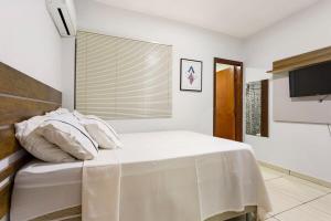 ein Schlafzimmer mit einem Bett mit weißen Laken und einem Fernseher in der Unterkunft Apartamentos Com Suite ,Wi-Fi 500MB , Estacionamento, Elevador, Cozinha Completa , Jr Catito in Brasilia