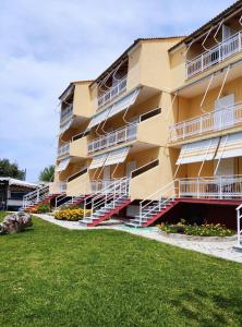 a yellow apartment building with white balconies and a yard at Acrogiali Rooms in Riza