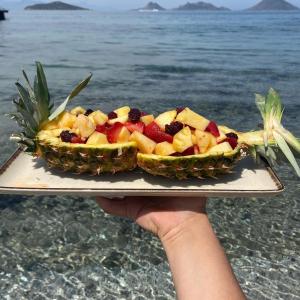 a person holding a plate of fruit on the beach at Small Beach Hotel in Turgutreis