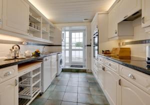 cocina con armarios blancos y suelo de baldosa en Flora Belle Cottage, en Sennen