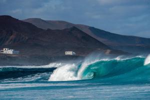 a large wave in the ocean with mountains in the background at Casa Rosaura in La Santa