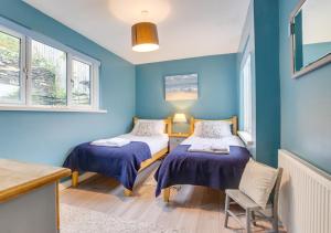 twee bedden in een kamer met blauwe muren en ramen bij Dawn End in Looe