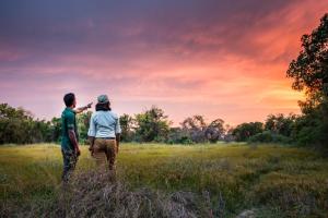 a man and woman standing in a field at sunset at Mahoora - Wilpattu by Eco Team in Wilpattu
