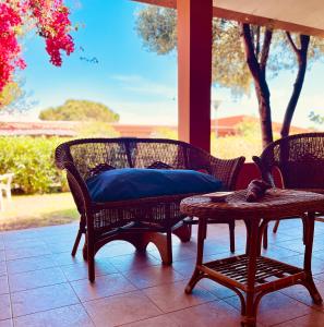 a porch with two wicker chairs and a table with a blue pillow at 20 steps from the beach VILLINO STECU in Costa Rei