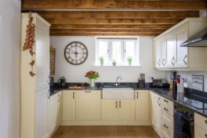una cocina con armarios blancos y un reloj en la pared en Mythra Cottage en Stokenham