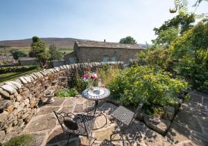 a patio with a table and chairs and a stone wall at Bizzys Bolthole in Reeth