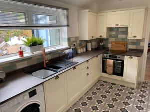 a kitchen with white cabinets and a sink and a dishwasher at Rhondda Tunnel Cottage by StayStaycations in Treorky
