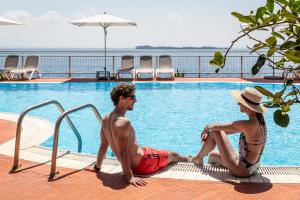 Ein Mann und eine Frau sitzen neben einem Pool in der Unterkunft Hotel Villa Florida & Suite Apartments in Gardone Riviera
