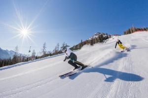 dwoje osób jeździ na nartach po pokrytym śniegiem stoku w obiekcie Sport Hotel Passo Carezza w mieście Vigo di Fassa