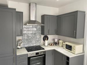 uma cozinha com armários cinzentos, um fogão e micro-ondas em Prospect Cottage by StayStaycations em Treorky
