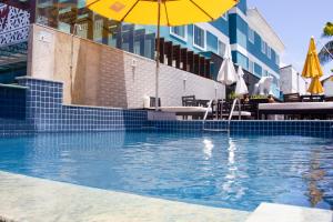 a swimming pool with an umbrella and tables and chairs at Pousada SUN Victory in Cabo Frio