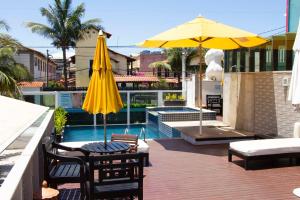 um pátio com um guarda-sol amarelo e cadeiras e uma piscina em Pousada SUN Victory em Cabo Frio