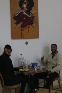dos hombres sentados en una mesa con un plato de comida en Hostel Juniors en Buenos Aires
