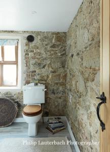 a bathroom with a white toilet and a stone wall at Kilquiggan Cottages in Coolkenna Street