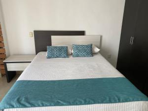 Apartamentos Frente a La Playa Boca del Rio في بوكاي ديل ريو: سرير مع اثنين من الوسائد الزرقاء ومكتب