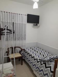 um quarto com uma cama, uma televisão e uma cadeira em Recanto Suítes em Araruama