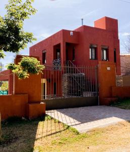 ein rotes Haus mit einem Zaun davor in der Unterkunft Bella Vista Casa con pileta y terraza in Villa Carlos Paz