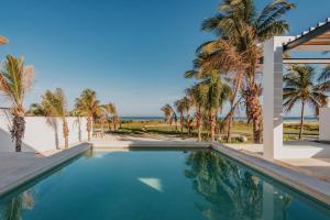 a swimming pool with palm trees and the ocean at Villa de lujo frente al mar de Progreso in Progreso