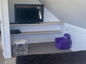 a living room with a tv and a purple chair at Bright Cosy Cottage in Whitianga