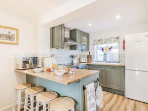 una cocina con armarios verdes y una barra con taburetes en Rosemary Cottage en Hickling