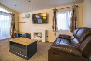 a living room with a leather couch and a fireplace at Luxury Platinum Lodge At Suffolk Sands Holiday Park Ref 45009mv in Felixstowe